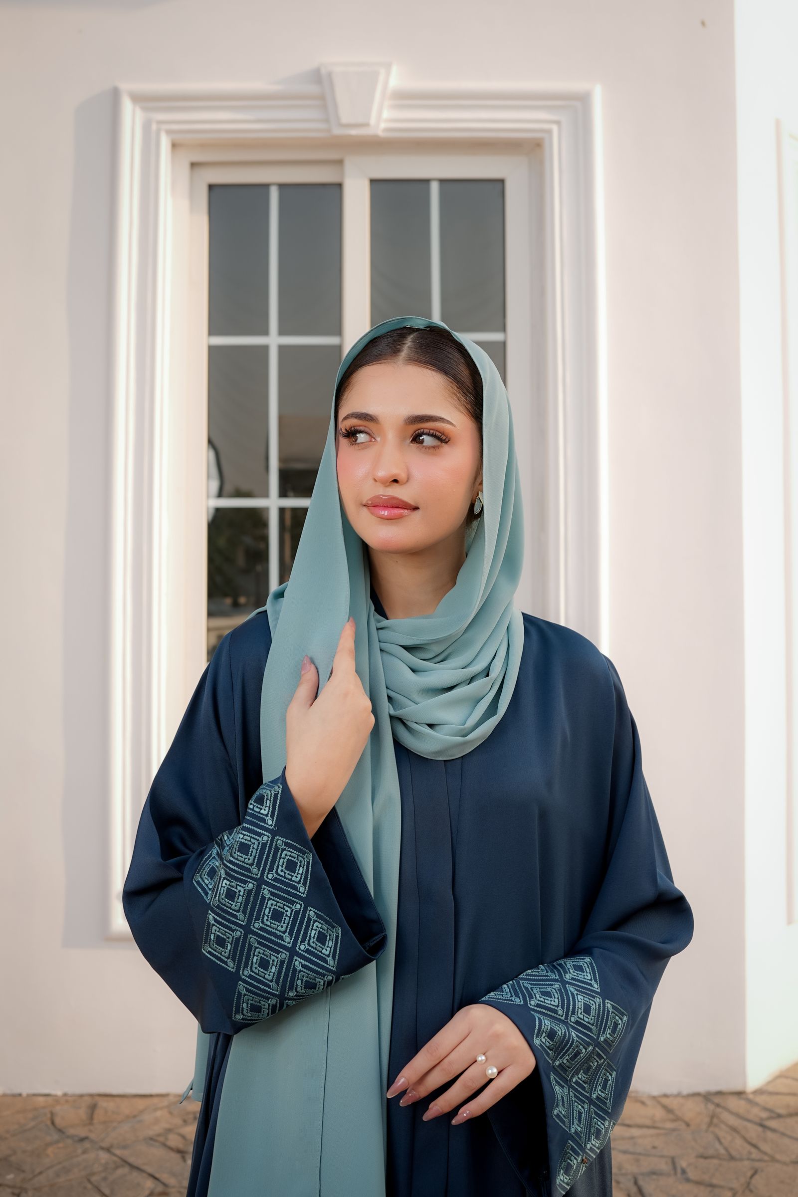 Model in a deep teal abaya with patterned cuffs